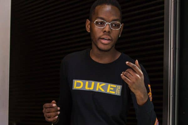 A young male usher wearing glasses and a sweatshirt gestures with hands in a doorway.