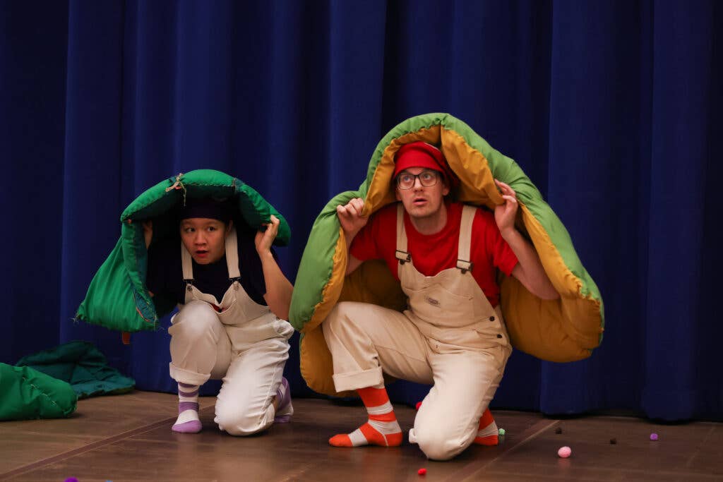 Two people wearing white overalls on one knee with a green pillow above them